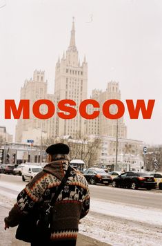 a man walking down the street in front of a tall building with a red moscow sign above it