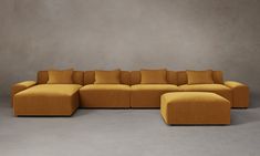 a yellow couch with pillows on it in front of a gray wall and grey floor