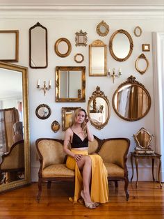 a woman sitting on a couch in front of a wall full of mirrors and furniture