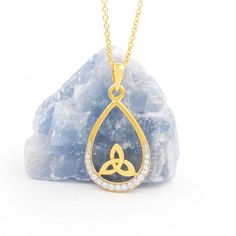 a gold necklace with an open tear shaped pendant hanging from it's side on top of a rock