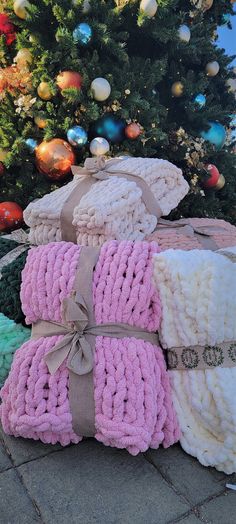 three knitted blankets stacked next to a christmas tree in front of a decorated christmas tree