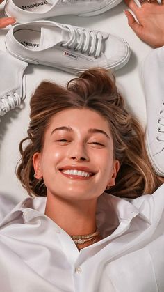 a woman laying on top of white shoes and smiling at the camera with her eyes closed