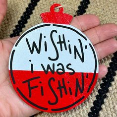 a hand holding a red and white ornament that says, wishin'i was fishin