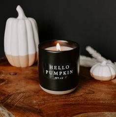 a black candle sitting on top of a wooden table next to white pumpkins and candles