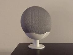 a close up of a white speaker on a black table with a gray wall in the background