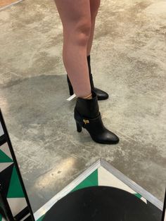 a woman's legs in high heeled black shoes standing on top of a tiled floor