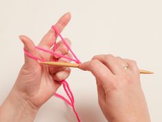 a woman is knitting with pink yarn and a wooden crochet hook in her hands