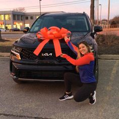 a woman kneeling down next to a car with a large bow on it