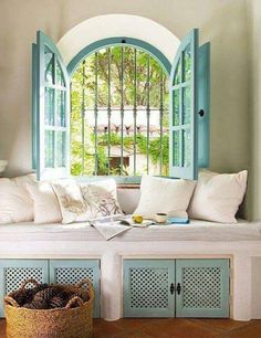 an arched window with blue shutters and pillows on the bench in front of it