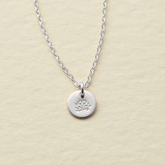 a silver necklace with a small flower charm on it's link, hanging from a white background