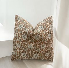 a brown and white flowered pillow sitting on top of a wooden floor next to a window