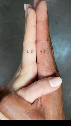 two hands holding each other with the word love tattooed on their thumbnails in front of them