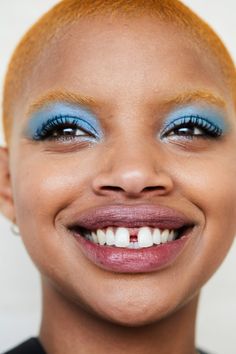 a close up of a person with blue eyeshadow and orange hair smiling at the camera