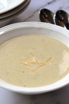 a white bowl filled with soup on top of a table next to silver spoons