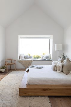 a bedroom with white walls and wooden flooring has a large window in the corner