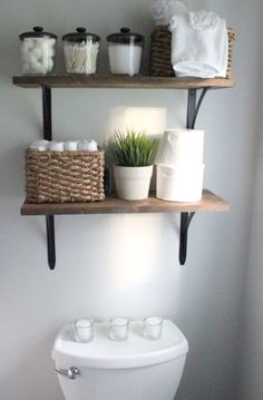 two shelves above a toilet with towels and cups on top of it, next to the toilet