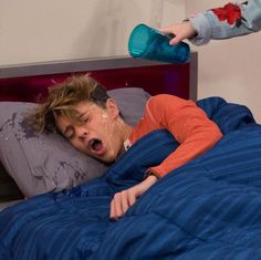 a young boy laying in bed with his mouth open and drinking water from a bottle