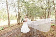 a woman in a wedding dress holding a veil over her head while walking through the woods