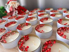 many white candles with red sprinkles are arranged on a table next to a santa clause