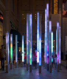 people are walking through an illuminated area in the middle of a building with columns on both sides