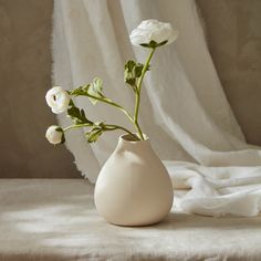 a white vase filled with flowers on top of a bed next to a window curtain