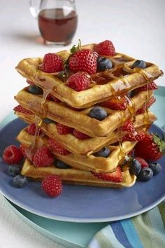 a stack of waffles topped with berries and syrup on top of a blue plate