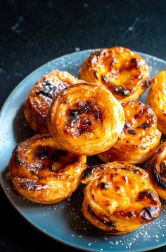 a plate full of cinnamon buns on top of a blue tablecloth with powdered sugar