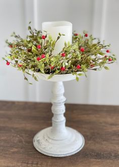 a white candle holder with red berries and greenery in it on a wooden table