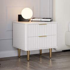 a white cabinet with two drawers and a lamp on it next to a chair in a room