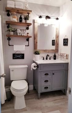 a white toilet sitting next to a bathroom sink under a wooden mirror mounted above it