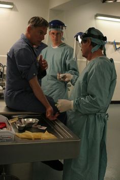 three people in scrubs standing around a table with food on it and one person wearing goggles