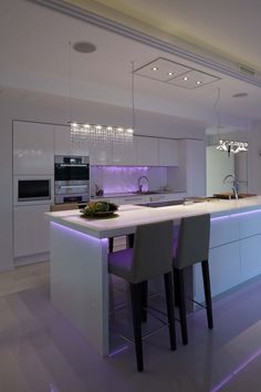 a modern kitchen with white cabinets and purple lights on the countertop, along with two bar stools