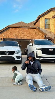 a man sitting on the ground in front of two parked cars next to each other