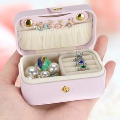 a hand holding an open jewelry box filled with rings and other accessories, including a ring case