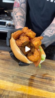 a man holding a hot dog with tater tots in his hand on top of a wooden table