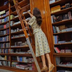 a woman climbing up the side of a wooden ladder in a book case filled with books