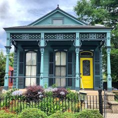 a blue house with a yellow door and black iron fence around the front yard area