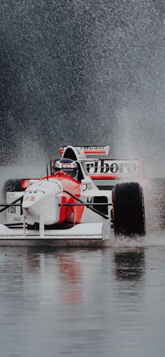 a man driving a race car in the water on a rainy day with splashes