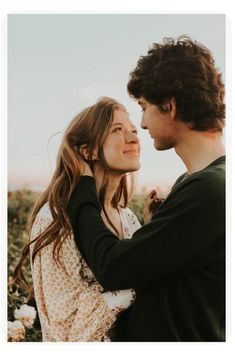 a man and woman are standing in a field with flowers looking into each other's eyes