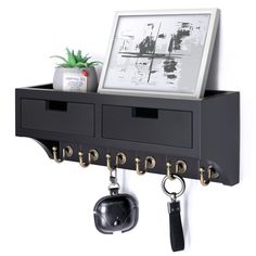 a black shelf with two drawers and keys hanging from it's hooks, next to a potted plant