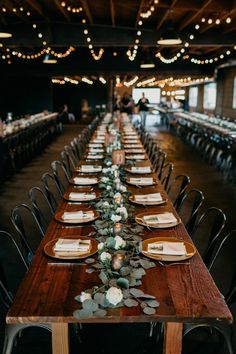 a long wooden table with place settings and greenery on the tables in front of it