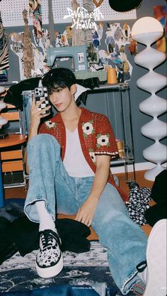 a young man sitting on top of a bed next to a pile of clothes and shoes