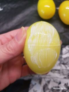 a person holding an egg in their hand with two yellow eggs behind them on a table