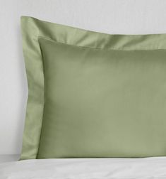 a green pillow on top of a bed with white sheets and pillows in the background