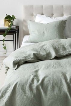 an unmade bed with green linens and pillows on the headboard, next to a plant