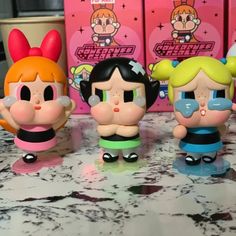 three little cartoon figures sitting next to each other on a counter top with pink boxes in the background