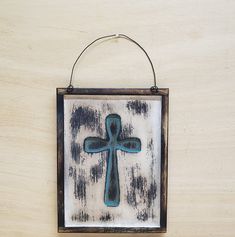 a blue cross hanging on a wall with a wood frame and metal loop around it