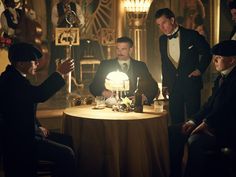 a group of men in tuxedos standing around a table with a cake on it