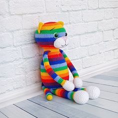 a crocheted cat sitting against a white brick wall in front of a wooden floor