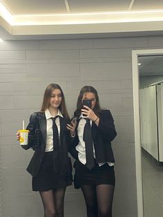 two young women standing next to each other in front of a mirror holding cell phones